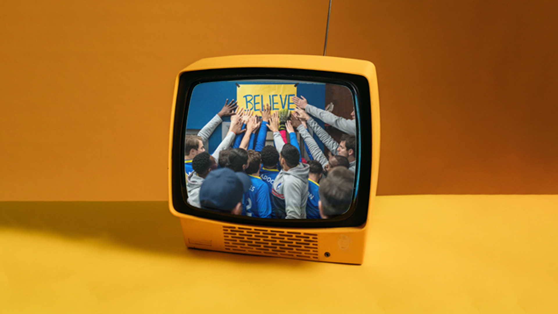 An image of a yellow television, on it is a still of the AFC Richmond team all touching the Believe sign in the changing room.